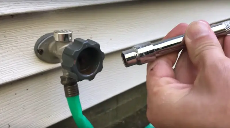 Using a 3/8" socket wrench to loosen the rusty bolt on the outdoor spigot
