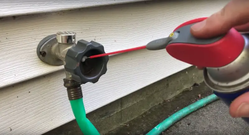 Spraying on WD-40 to loosen the rusty bolt on the outdoor faucet