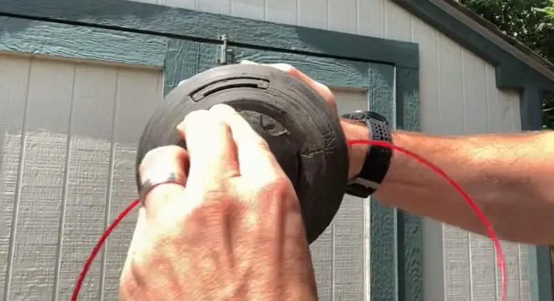 Rotating the central disc of the trimmer head to wind in the line