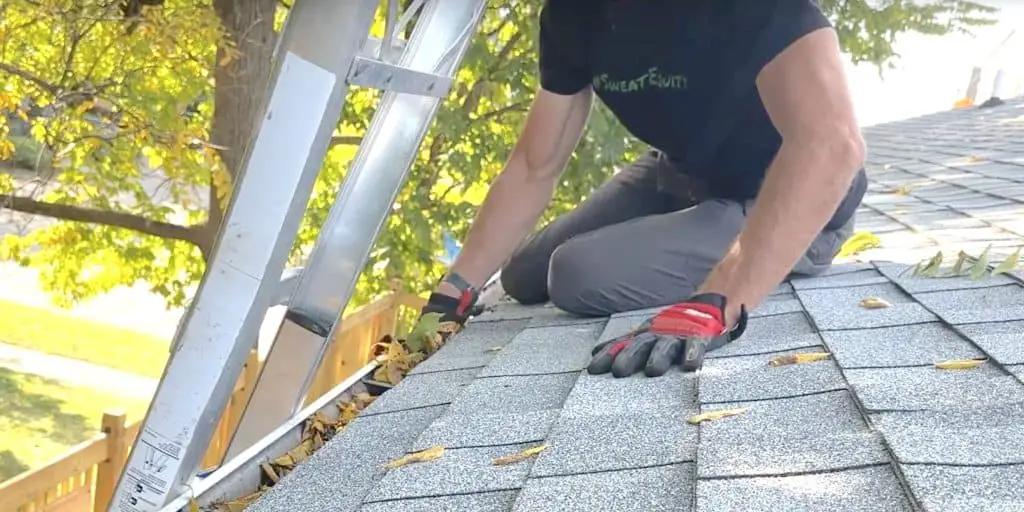 Clearing out gutters by scooping debris into a bucket